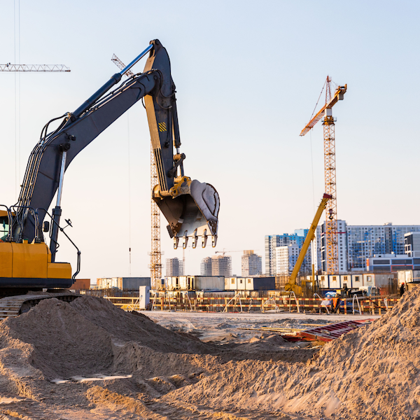 A construction site at sunset featuring a yellow excavator with its arm extended over a pile of sand.