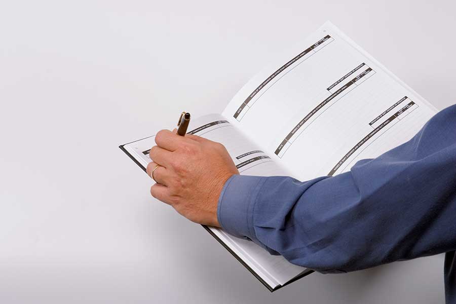 A person in a blue shirt writing in a Log Book