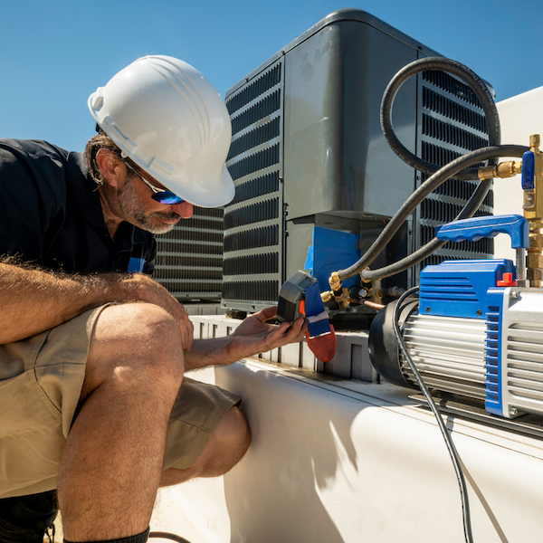 The image depicts a technician wearing a white hard hat and sunglasses, working on a mechanical unit.