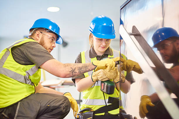 A young apprentice carpenter being supervised by her co-worker. They are wearing safety workwear.