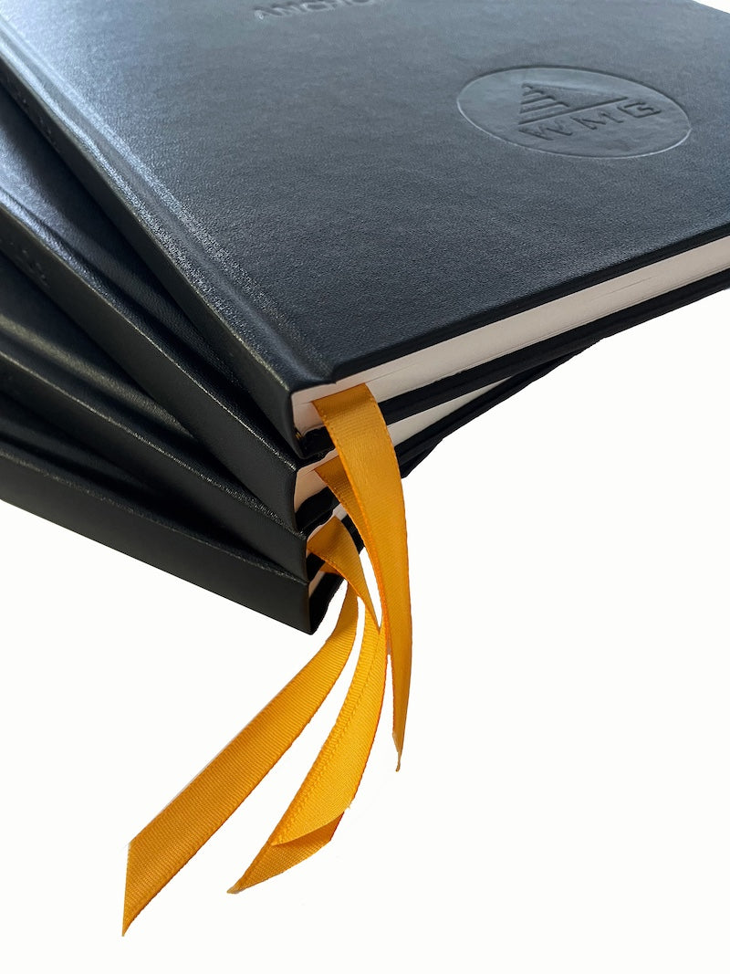 a stack of four black log books with an orange placeholder sticking out from the bottom