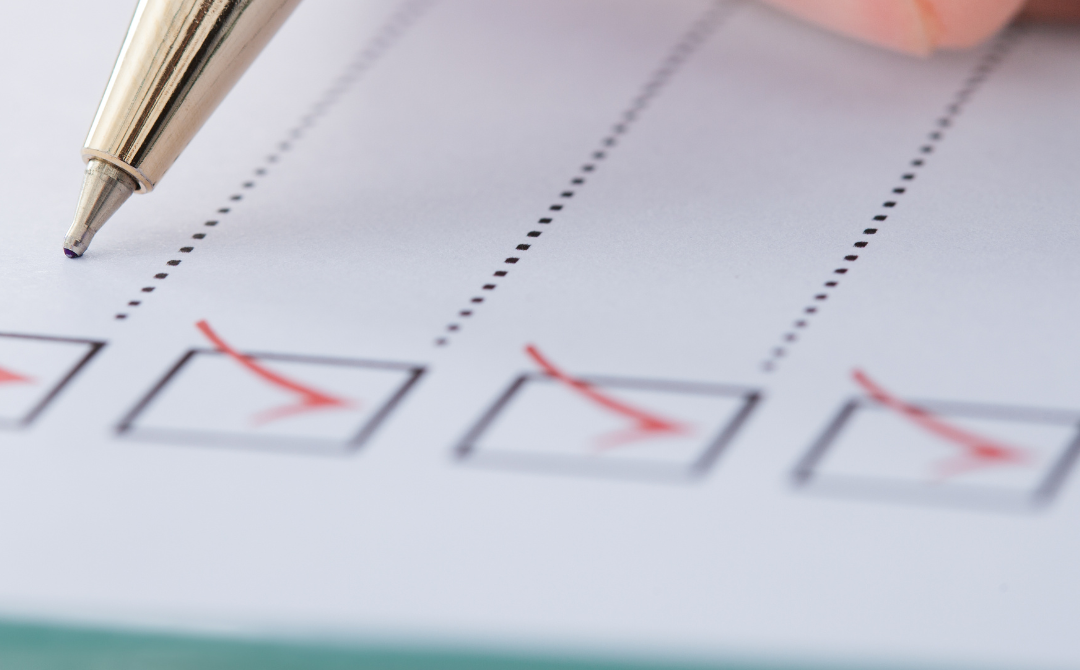 A close-up of a hand holding a pen, marking checkboxes on a checklist with red ink.